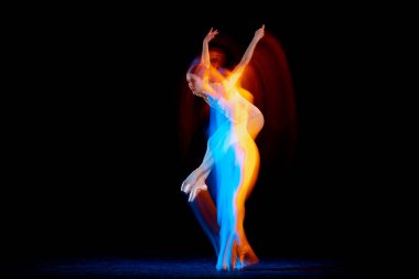 Ease of movement. Tender female ballet dancer dancing solo dance over dark background in mixed neon light. Art, flexibility, inspiration and beauty concept. Moves in fire glow. Copy space for ad