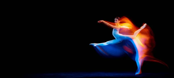 Ease of movement. Tender female ballet dancer dancing solo dance over dark background in mixed neon light. Art, flexibility, inspiration and beauty concept. Moves in fire glow. Copy space for ad