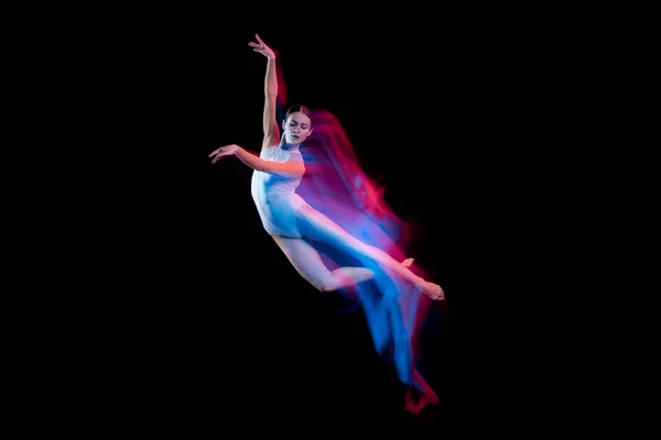 Ease of movement. Tender female ballet dancer dancing solo dance over dark background in mixed neon light. Art, flexibility, inspiration and beauty concept. Moves in fire glow. Copy space for ad