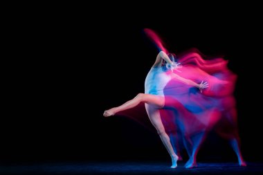 Ease of movement. Tender female ballet dancer dancing solo dance over dark background in mixed neon light. Art, flexibility, inspiration and beauty concept. Moves in fire glow. Copy space for ad