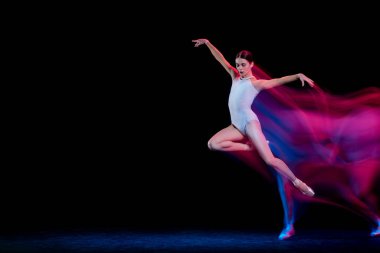 Music. Graceful ballerina dancing on dark background in mixed neon light. Art, fashion, grace, movement, action and motion concept. Looks weightless, flexible. Copy space for ad