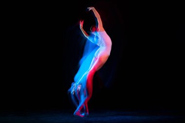 Flight. Tender female ballet dancer dancing solo dance over dark background in mixed neon light. Art, flexibility, inspiration and beauty concept. Moves in fire glow. Copy space for ad