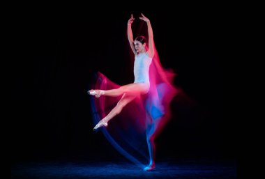 Ease of movement. Tender female ballet dancer dancing solo dance over dark background in mixed neon light. Art, flexibility, inspiration and beauty concept. Moves in fire glow. Copy space for ad