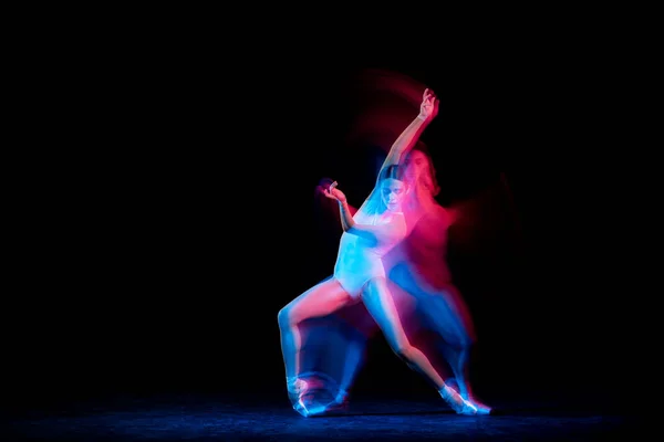 Music. Graceful ballerina dancing on dark background in mixed neon light. Art, fashion, grace, movement, action and motion concept. Looks weightless, flexible. Copy space for ad