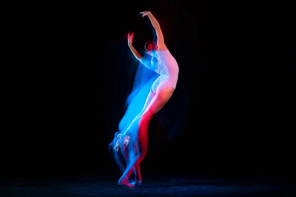 Flight. Tender female ballet dancer dancing solo dance over dark background in mixed neon light. Art, flexibility, inspiration and beauty concept. Moves in fire glow. Copy space for ad