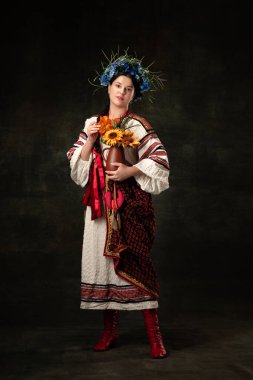 Free and beauty. Art portrait of beautiful woman wearing traditional folk Ukrainian costume posing isolated over dark vintage background. Fashion, beauty, cultural heritage concept.