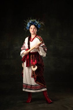 Freedom and independence. Art portrait of beautiful woman wearing traditional folk Ukrainian costume posing isolated over dark vintage background. Fashion, beauty, cultural heritage concept.