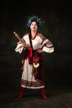 Fight for womens rights. Emotional adorable woman wearing national folk Ukrainian attire posing isolated over dark vintage background. Fashion, beauty, cultural heritage concept.