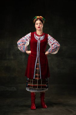 Freedom and independence. Art portrait of beautiful woman wearing traditional folk Ukrainian costume posing isolated over dark vintage background. Fashion, beauty, cultural heritage concept.