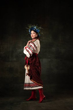Freedom and independence. Art portrait of beautiful woman wearing traditional folk Ukrainian costume posing isolated over dark vintage background. Fashion, beauty, cultural heritage concept.