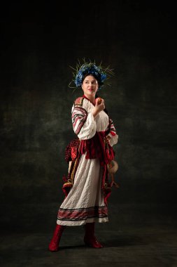Freedom and independence. Art portrait of beautiful woman wearing traditional folk Ukrainian costume posing isolated over dark vintage background. Fashion, beauty, cultural heritage concept.