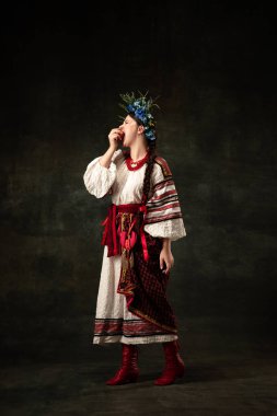 Freedom and independence. Art portrait of beautiful woman wearing traditional folk Ukrainian costume posing isolated over dark vintage background. Fashion, beauty, cultural heritage concept.