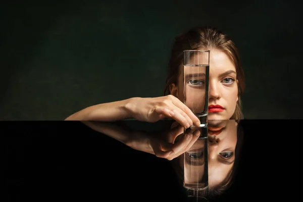 Contemporary art portrait of pretty girl looking through glass of water. Object distortion, optical illusion. Concept of art, creativity, surrealism. Weird emotions, facial expression concept.