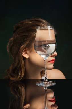 Huge eye. Creative art photography. Closeup girls face through wine glass over dark background. Object distortion, optical illusion. Minimalistic contemporary art. Poster