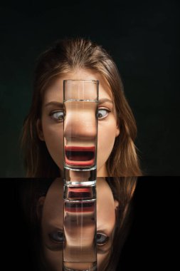 Crazy. Creative art photography. Stylish girls face through wine glass over dark green background. Object distortion, optical illusion. Minimalistic contemporary art. Poster