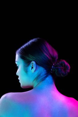 Back view of young beautiful girl well-kept skin posing isolated over dark background in purple neon light. Spa, fashion, beauty, health, body and skin care concept.