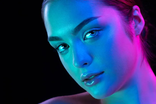 Closeup young beautiful woman with well-kept skin and sophisticated facial features isolated over dark background in purple neon light. Concept of art, fashion, style, inspiration, emotions.