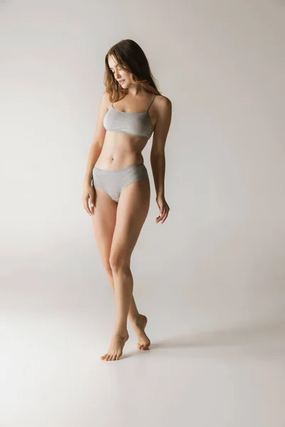 Femininity. Young beautiful slim woman in grey cotton underwear isolated over gray background. Wellness, wellbeing, fitness, diet and aesthetic cosmetology concept. Natural beauty of female body