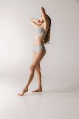 Femininity. Young beautiful slim woman in grey cotton underwear isolated over gray background. Wellness, wellbeing, fitness, diet and aesthetic cosmetology concept. Natural beauty of female body