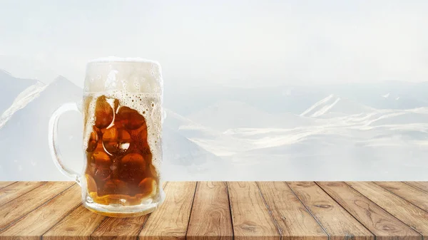 Large beer mug with light cold beer standing on wooden table over snow-capped mountains background. Holidays, vacation, drinks, taste, ad and oktoberfest concept. Design for wallpaper