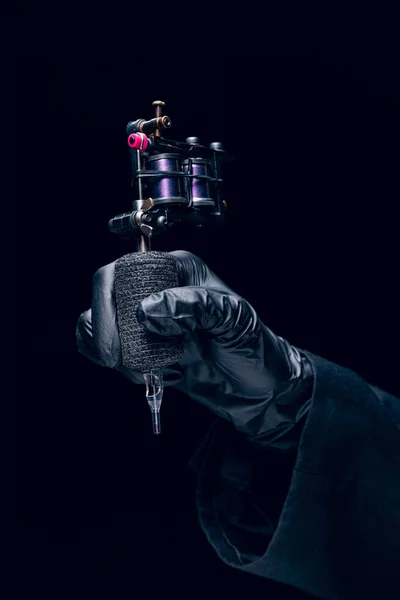 Machine for tattoo. Human hand in black protective glove holding professional equipment for making tattoo on body isolated on dark background. Concept of art, job, hobby, poster for ad