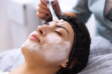 Besleyici bir maske takıyorum. Güzellik muayenehanesinde estetik ameliyatlar sırasında genç ve güzel bir kız. Güzellik, cilt bakımı, nemlendirici, beslenme, gençleştirme konsepti.