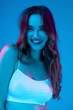 Kıvırcık uzun saçlı, gülümseyen ve mutlu ve rahat bir yüz ifadesiyle kameraya bakan neşeli, güzel bir kızın yarım boy portresi. Sağlık, güzellik, moda ve reklam kavramı