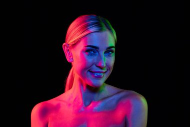 Moda, tarz. İyi korunmuş derisi ve şık makyajı olan genç ve güzel bir kadın. Pembe neon ışıkta koyu bir arka planda izole edilmiş. Doğal güzellik, sanat, duygu, kozmetik ve gençlik kavramı