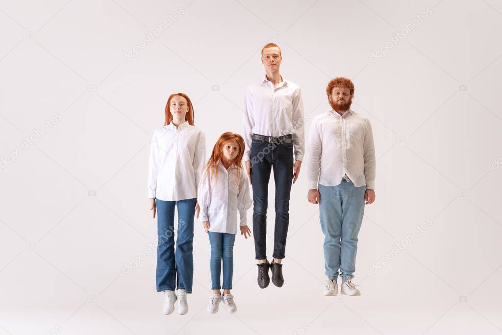 Levitation and calmness. Two men and woman and kid, red-headed young people wearing casual style clothes flighting over white background. Creativity, inspiration, art, fashion, emotions, style.