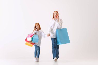 Meşgul bayanlar. Güzel, genç, kızıl saçlı anne ve kız beyaz arka planda izole edilmiş alışveriş torbalarıyla alışverişe gidiyorlar. Kara Cuma kavramı, siber pazartesi, satış