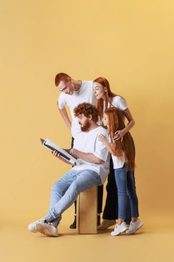 Haberler. Farklı yaşlarda, beyaz tişört ve kot giyen kızıl saçlı insanlar sarı arka planda izole edilmiş poz veriyorlar. Duygular, dostluk ve aktif yaşam tarzı. Mutlu, mutlu ve sevimli görün.