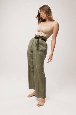 İçim rahat olsun. Uzun kıvırcık saçlı, doğal makyajlı, uzun etekli ve beyaz arka planda poz veren sıradan pantolonlu güzel bir kızın stüdyo fotoğrafı. Kadın vücudunun doğal güzelliği