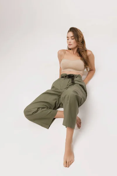 Peace of mind. Studio shot of pretty young girl with long curly hair and natural makeup wearing crop top and casual trousers posing over white background. Natural beauty of female body