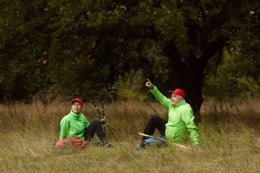 Dinlenme zamanı. Yaşlılar, kadın ve erkek sporcu üniforması içinde güneşli bir günde, açık havada sonbahar ormanlarında yürüyüş yapıyorlar. Spor anlayışı, fitness, hobiler, İskandinav yürüyüşü ve sağlıklı yaşam tarzı. Mutlu görün.