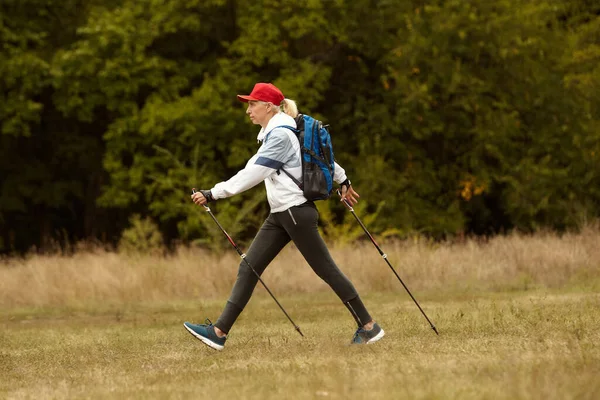 Energy. Active sportive elderly woman practicing in Nordic walking with sticks in public park, outdoors. Autumn sports, healthy lifestyle. Concept of sport, body care, action