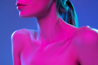 Close up female neck, collarbones and shoulders in pink neon light over dark background. Beautiful young womans body with well-kept skin. Beauty, fitness, diet, spa, aesthetic cosmetology