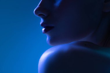 Gece hayatı. Koyu mavi arka planda neon ışıklı genç bir kadının kırpılmış görüntüsü. Tek renkli olsun. Siber punk tarzı, güzellik, kozmetik konsepti. Ciddi ve düşünceli.