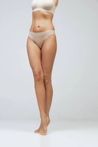 腿和臀部 用灰色背景隔离的内衣剪裁了年轻女性晒黑身体的图像 自然美概念 体重减轻 — 图库照片