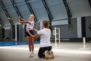 Takım çalışması, sonuç stratejisi. Küçük kızlar, spor salonunda spor aletleriyle egzersiz yapan yeni başlayan jimnastik sporcuları. Öğrenim kavramı, başarılar, yetenekler. Koç ile ders.
