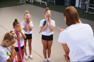 Çalışma ve eğitim metodu. Küçük kızlara öğretmenlik yapan genç bir kadın spor salonunda, iç mekanda yeni başlayan jimnastik sporcuları. Spor anlayışı, başarılar, öğrenim, hedefler, beceriler