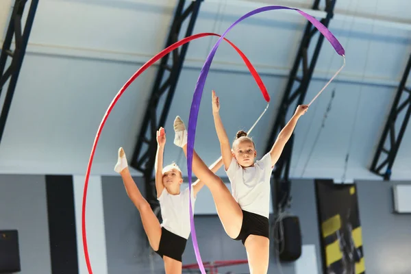 Beauty of movement, confidence in victory. Two little girls, female rhythmic gymnast training with colorful ribbons at sport gym, indoors. Concept of action, motion, sport, motivation, competition.