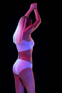 Selülitsiz güzel duruş ve kalçalar. Siyah arka planda, neon ışıkta izole edilmiş iç çamaşırlı genç Seansual kadın. Sağlık, kilo kaybı, tedavi, sağlık hizmetleri, fitness