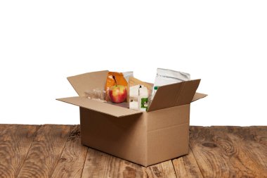 Yumurta, yağ, paketlenmiş yiyecek ve beyaz zemin üzerinde duran ahşap masanın üzerinde duran çeşitli yiyecek parçalarıyla dolu karton bir kutu aç. Bağışlar, bağışlar. Yardım programı, mültecilere destek, göçmenler. Sosyal konular