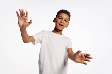 Öğrenci çocuk ellerini kameraya sallıyor. Beyaz tişörtlü Afrikalı küçük bir çocuğun yarım boy portresi beyaz arka planda izole edilmiş duygularını ifade ediyor. Çocuk duyguları, mutlu çocukluk kavramı