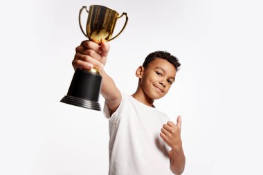 Kazandım. Beyaz tişörtlü mutlu Afrikalı çocuk beyaz arka planda izole edilmiş kameraya ödülünü gösteriyor. Çocuk duyguları, öğrenim, başarılar, beceriler, kazanma konsepti