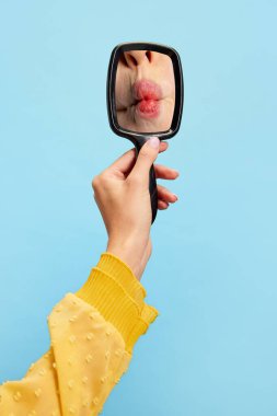 Balık suratı yapıyorum. Kadınların elleri, mavi arka planda izole edilmiş dişi kırmızı dudakların yansıması olan küçük aynayı tutuyor. Eski moda, eski tarz, güzellik, reklam..