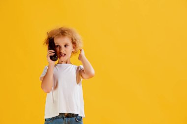 Geçmişe çağrı. Küçük tatlı bir kız, sarı arka planda izole edilmiş eski cep telefonu kullanan bir çocuk. Çocuk duyguları, moda, güzellik kavramı, çağlar karşılaştırması. İlan için alanı kopyala