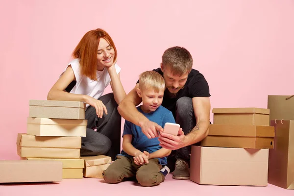 Confirm order. Happy mother, father and son open cardboard boxes, receive parcels unpack after online shopping over pink background. Unbox package, post shipping delivery and big sales day concept