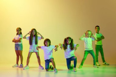 Dans dersi, hip-hop, tefekkür koreografisi. Neşeli çocuklar, tişörtlü çocuklar ve hareket halinde dans eden kot pantolonlar sarı neon ışıkta yeşil arka planda izole edilmiş. Müzik, moda, sanat kavramı