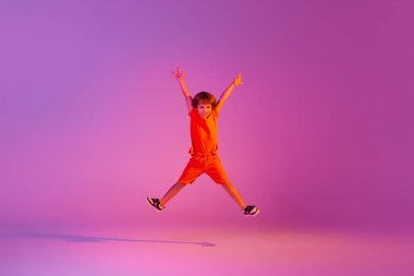 Uçuş. Etkileyici küçük bir kız, parlak elbiseli bir çocuk pembe arka planda izole bir şekilde zıplıyor. Çocuk duyguları, haberler, zorluklar, çocukluk, eğitim kavramı. İlan için alanı kopyala